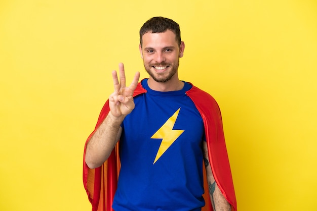黄色の背景に分離されたスーパーヒーローブラジル人男性幸せと指で3を数える
