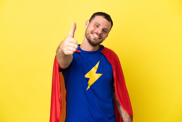 Super Hero Brazilian man isolated on yellow background shaking hands for closing a good deal