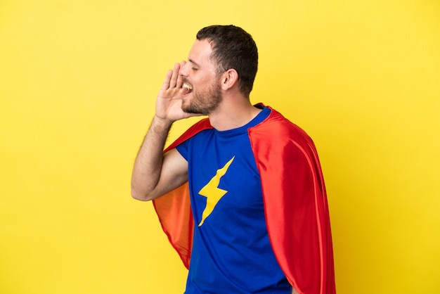 Super Hero Brazilian man isolated on yellow background shouting with mouth wide open to the lateral