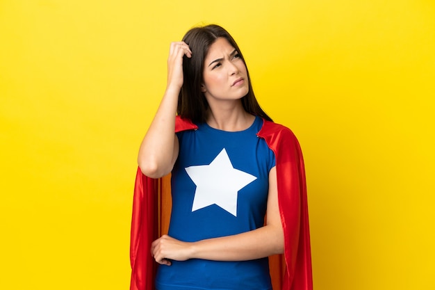 Super Hero Brazilian woman isolated on yellow background having doubts and with confuse face expression