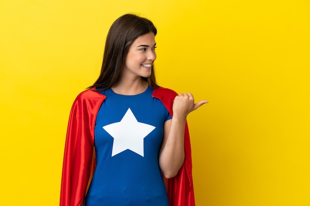 Photo super hero brazilian woman isolated on yellow background pointing to the side to present a product