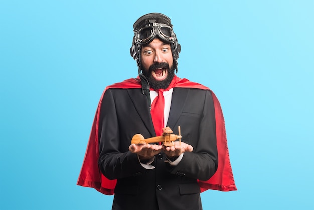 Super hero businessman holding a wooden toy airplane on colorful background