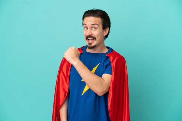 Super Hero caucasian man isolated on blue background celebrating a victory