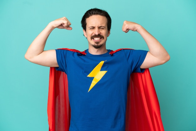 Super Hero caucasian man isolated on blue background doing strong gesture