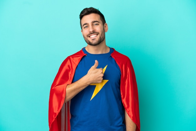 Super Hero caucasian man isolated on blue background giving a thumbs up gesture