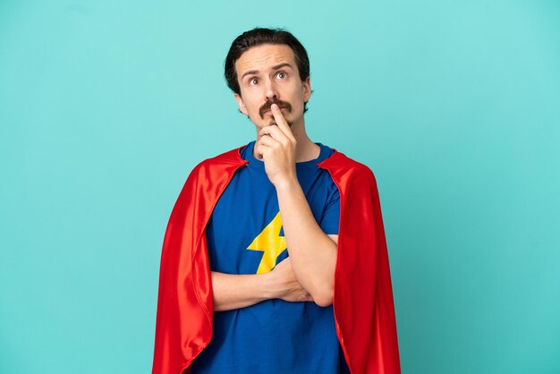 Super Hero caucasian man isolated on blue background having doubts while looking up