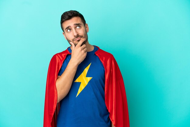 Super Hero caucasian man isolated on blue background having doubts and with confuse face expression