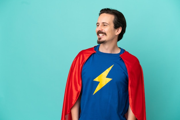 Super Hero caucasian man isolated on blue background looking to the side and smiling