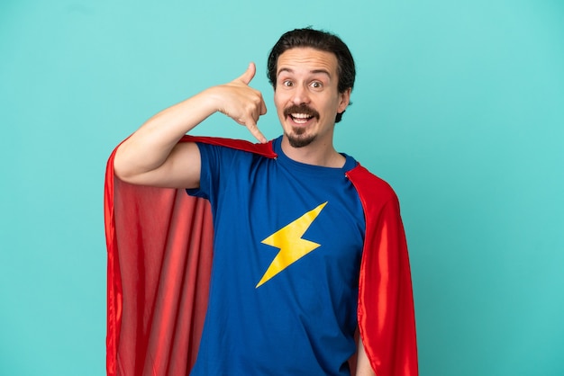 Super Hero caucasian man isolated on blue background making phone gesture. Call me back sign