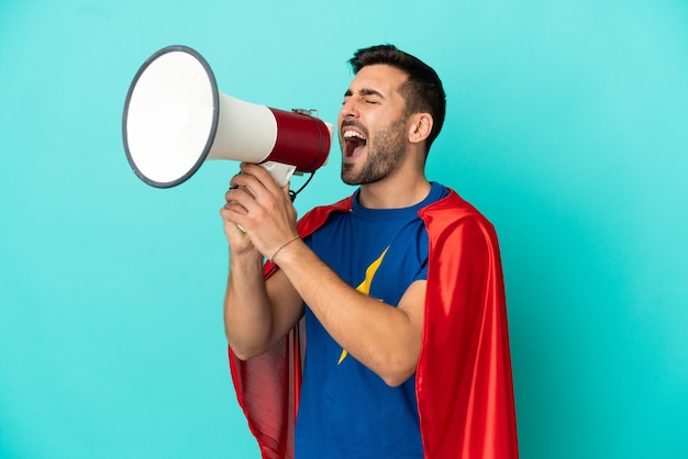 Super Hero caucasian man isolated on blue background shouting through a megaphone