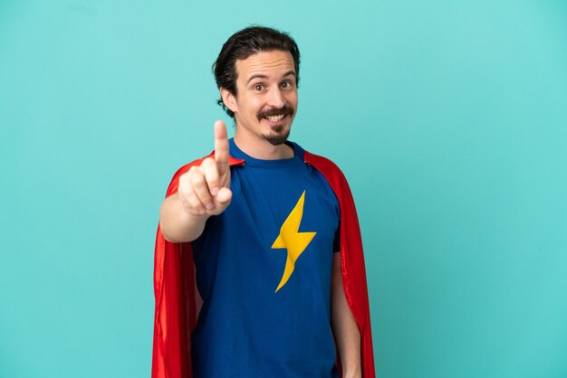 Super Hero caucasian man isolated on blue background showing and lifting a finger