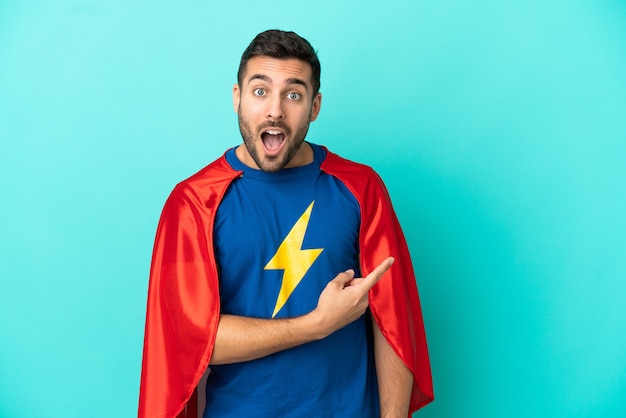 Super Hero caucasian man isolated on blue background surprised and pointing side