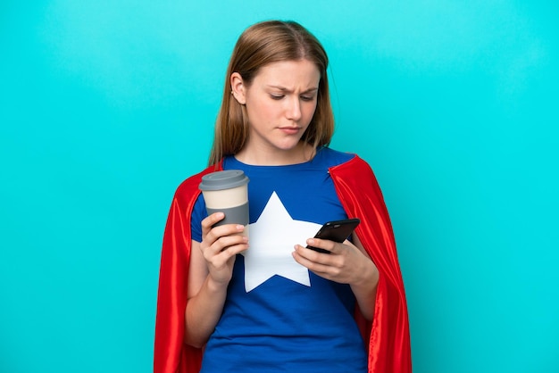 Super Hero caucasian woman isolated on blue background holding coffee to take away and a mobile