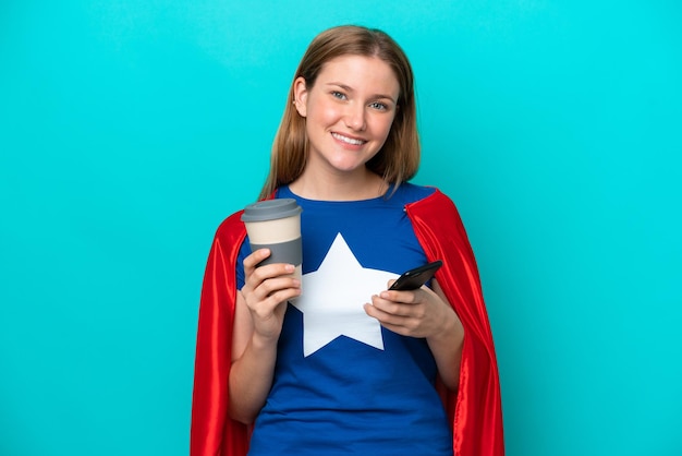 Super hero caucasian woman isolated on blue background holding coffee to take away and a mobile