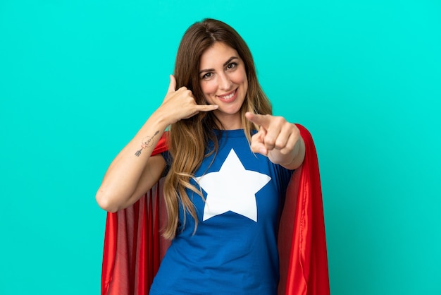 Super Hero caucasian woman isolated on blue background making phone gesture and pointing front