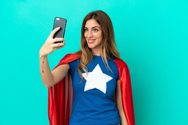 Super Hero caucasian woman isolated on blue background making a selfie