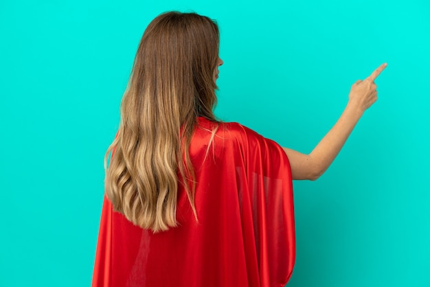 Super Hero caucasian woman isolated on blue background pointing back with the index finger