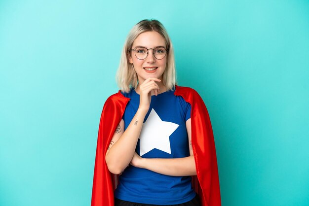 Super hero caucasian woman isolated on blue background with\
glasses and smiling
