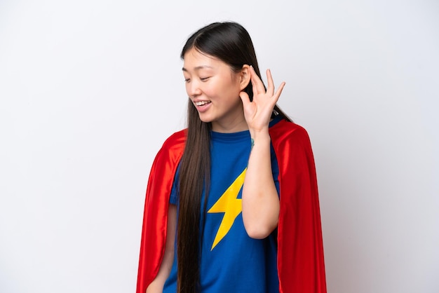Super Hero Chinese woman isolated on white background listening to something by putting hand on the ear