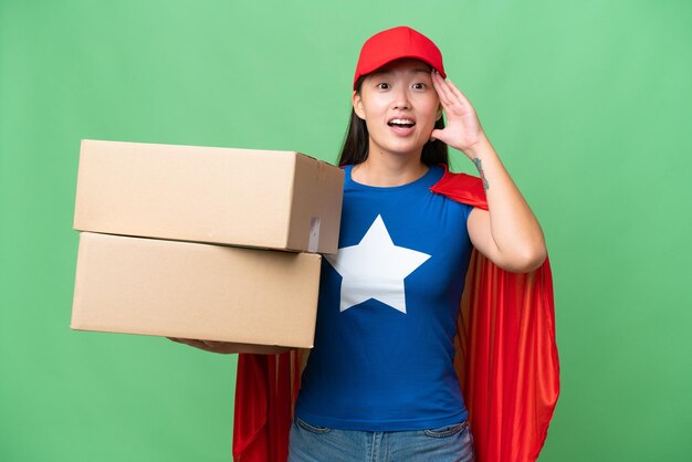 Super Hero delivery Asian woman holding boxes over isolated background with surprise expression