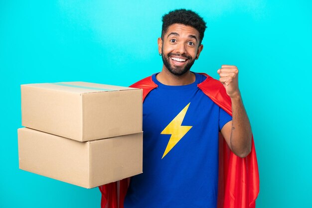 Super Hero delivery Brazilian man isolated on blue background celebrating a victory in winner position