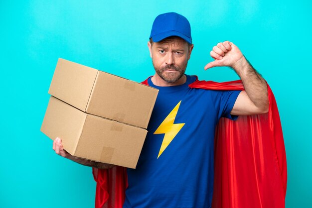 Uomo di consegna del super eroe isolato su sfondo blu che mostra il pollice verso il basso con un'espressione negativa