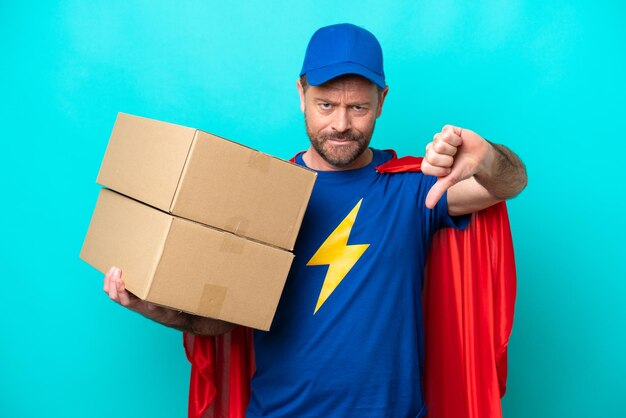 Photo super hero delivery man isolated on blue background showing thumb down with negative expression