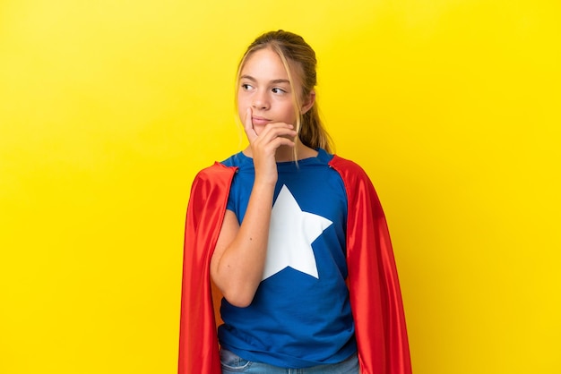 Super Hero little girl isolated on yellow background having doubts and with confuse face expression