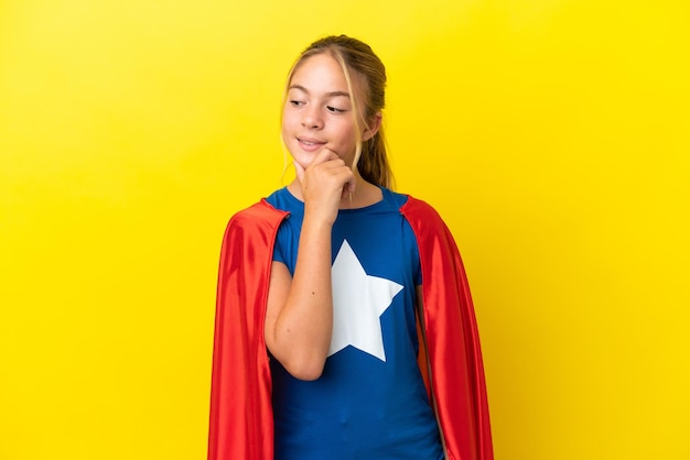 Super Hero little girl isolated on yellow background looking to the side