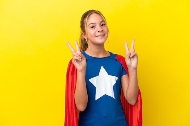 Foto bambina super hero isolata su sfondo giallo che mostra il segno di vittoria con entrambe le mani