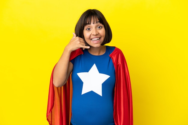 Super Hero pregnant woman isolated on yellow background making phone gesture. Call me back sign