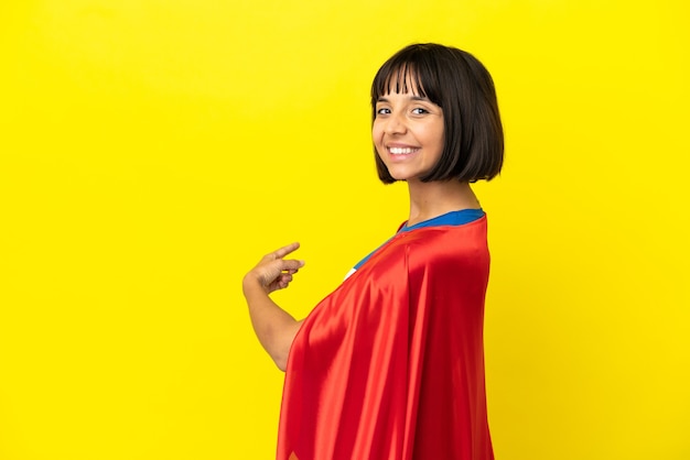 Super Hero pregnant woman isolated on yellow background pointing back