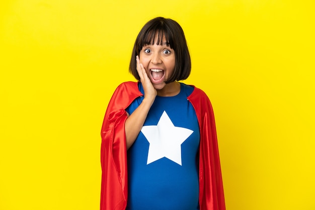 Super Hero pregnant woman isolated on yellow background with surprise and shocked facial expression