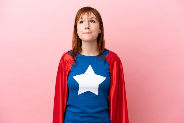 Super Hero redhead girl isolated on pink background and looking up