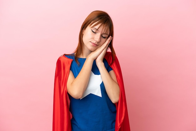 Super Hero redhead girl isolated on pink background making sleep gesture in dorable expression