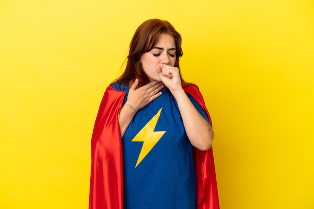 Super Hero redhead woman isolated on yellow background is suffering with cough and feeling bad