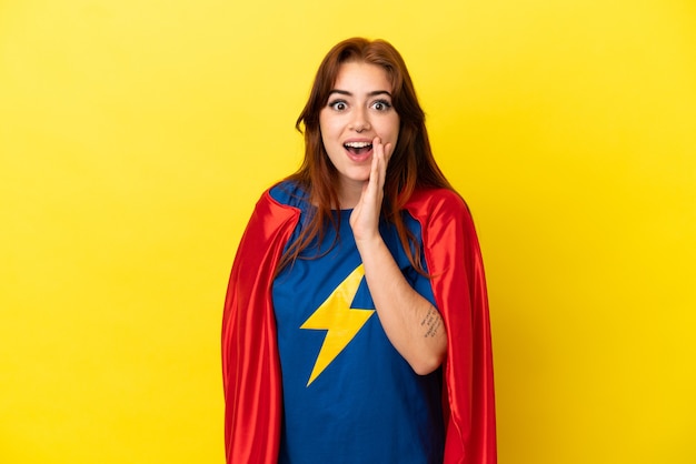 Super Hero redhead woman isolated on yellow background with surprise and shocked facial expression