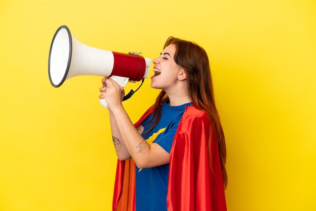 Super Hero roodharige vrouw geïsoleerd op gele achtergrond schreeuwen door een megafoon