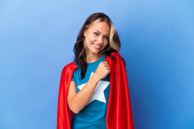 Super Hero Teenager girl isolated on blue background celebrating a victory