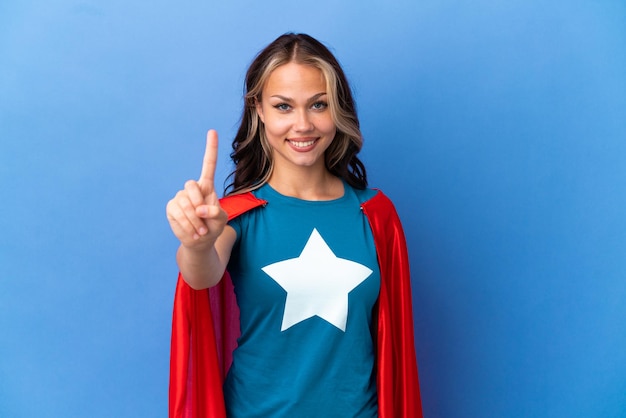 Super Hero Teenager girl isolated on blue background showing and lifting a finger