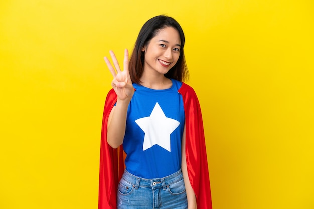 Super hero Vietnamese woman isolated  on yellow background happy and counting three with fingers