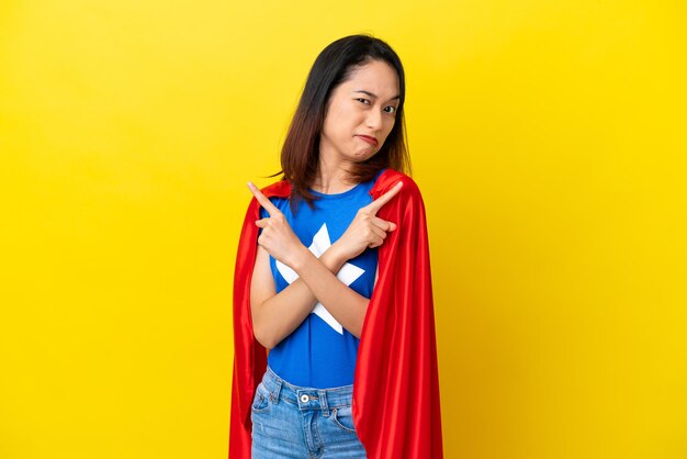 Super hero vietnamese woman isolated on yellow background\
pointing to the laterals having doubts