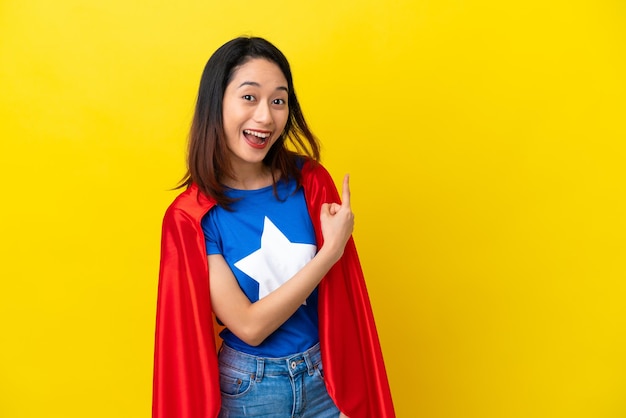 Super hero Vietnamese woman isolated  on yellow background surprised and pointing side