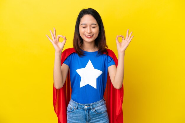 Super hero Vietnamese woman isolated  on yellow background in zen pose