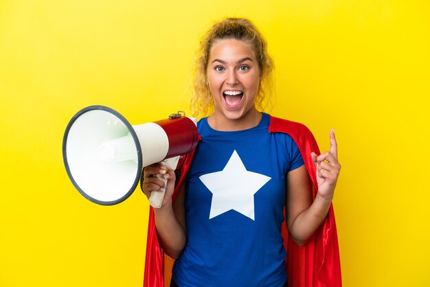 Foto super hero-vrouw geïsoleerd op een gele achtergrond die een megafoon vasthoudt en een geweldig idee naar boven wijst