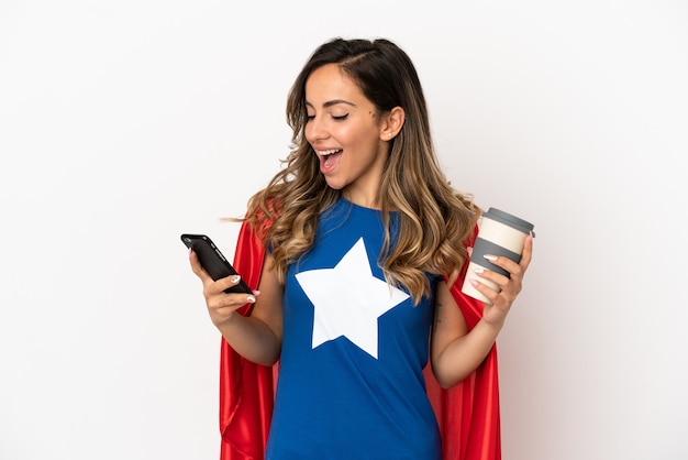 持ち帰り用のコーヒーと携帯電話を保持している孤立した白い背景の上のスーパーヒーローの女性