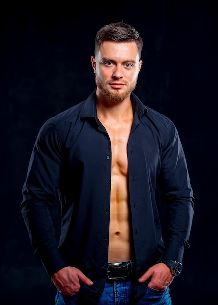 Super sexy man with tan abs and chest Athletic man with unbuttoned dark shirt on gray background Studio portrait