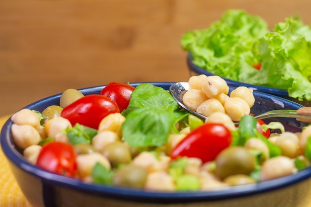 テーブルの上の青いボウルにオリーブとトマトの葉とひよこ豆とスプーンのスーパークローズ