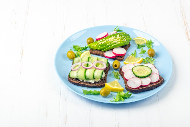 Superfood open vegetarische sandwich met verschillende toppings: avocado, komkommer, radijs op blauw bord. Gezond eten. Biologisch en vegetarisch eten. Detailopname,