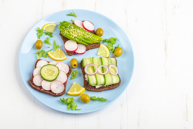 Superfood open vegetarische sandwich met verschillende toppings: avocado, komkommer, radijs op blauw bord op witte achtergrond. Gezond eten.